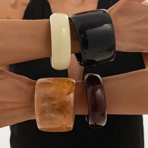 Primer plano de brazaletes de resina retro gruesos jaspeados y de colores sólidos en muñecas