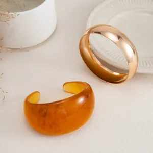 Pareja de brazaletes anchos de resina ámbar y metal dorado pulido sobre blanco.