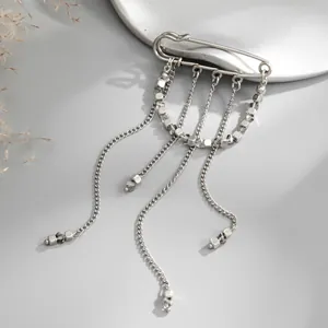 Détail d'une broche épingle de sûreté argentée avec des chaînes pendantes et des perles cubes