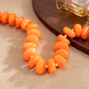 Detailansicht einer klobigen orangefarbenen Harzperlenkette mit goldenen Abstandsperlen.