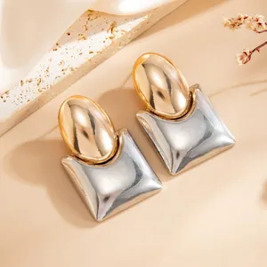 Nahaufnahme von minimalistischen zweifarbigen Metallohrringen mit Quadrat und Kugel.