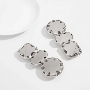 Close-up detail of silver geometric mirrored drop earrings with oval and round segments.
