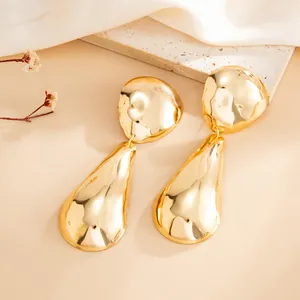 Detailed close-up of chunky gold-tone teardrop earrings with a hammered mirror finish.