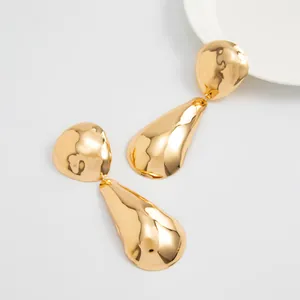 Detailed close-up of oversized gold geometric mirror earrings with hammered texture.
