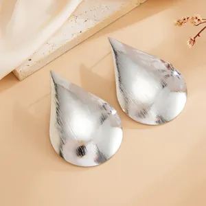 Close-up detail of large silver teardrop stud earrings with brushed mirror finish surface