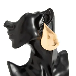 Detailed close-up view of large shiny gold teardrop stud earring on a black mannequin