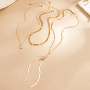 Détail de colliers dorés superposés avec chaîne serpent plate, gland et pendentif cristal