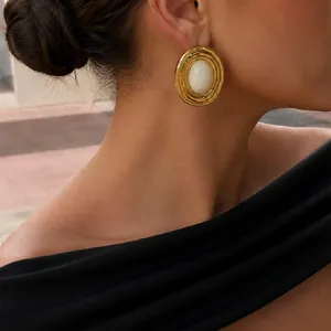 Primo piano di orecchini ovali placcati oro con inserto in resina bianca stile vintage.