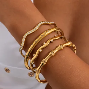 Gros plan d'un ensemble de joncs ondulés et d'un bracelet bambou en acier doré 18 carats