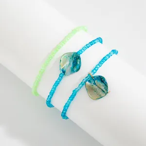 Detailed view of bohemian turquoise and lime green seed bead anklets with shell pendants.