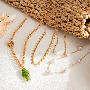 Gros plan détaillé de colliers dorés superposés avec pendentif poisson vert et perles