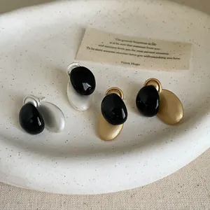 Vista detallada de pendientes de metal ovalados con un diseño único de esmalte negro.