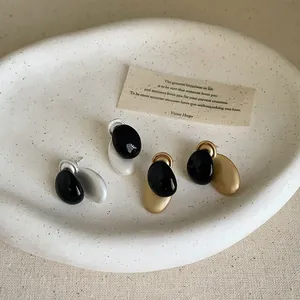 Detalle de pendientes de botón ovales de metal bicolor con esmalte negro en bandeja