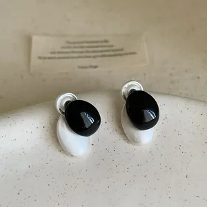 Primer plano de pendientes de botón ovalados minimalistas en esmalte blanco y negro.