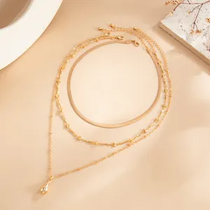 Détail du collier triple rang doré avec chaîne serpent et pendentif goutte d'eau.