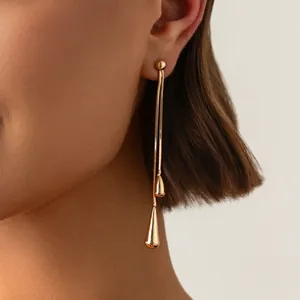 Nahaufnahme eleganter goldener langer Quastenohrringe mit Wassertropfen am Modell