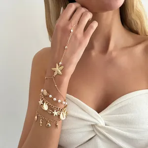 Vista detallada del brazalete de mano bohemio con estrellas de mar, conchas y perlas oro.