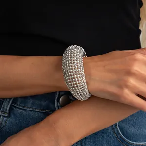 Dettaglio di un bracciale a polsino vintage in maglia d'argento intrecciata sul polso.