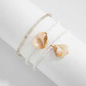 Close-up detail of bohemian white beaded anklets featuring natural shell pendants