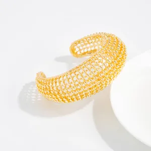 Vista dettagliata del bracciale rigido dorato traforato a maglia con trama perlata