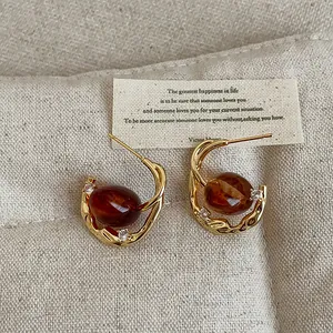 Close-up of vintage amber oval resin earrings with gold-textured metal and zircon stones.