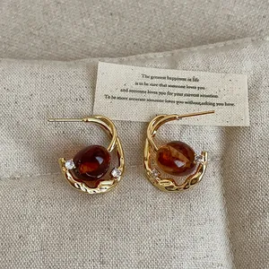 Close-up of elegant amber oval resin earrings with gold metal texture and small crystals
