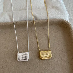 Detalle del colgante con diseño de bolso trenzado en acabados oro y plata.
