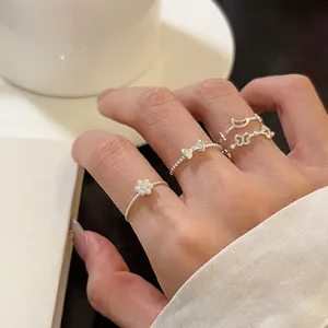 Close-up of delicate silver bow and flower rings worn on a hand, sweet and minimalist style.
