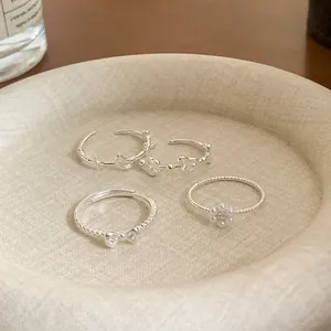 Detailed macro view of four dainty silver rings with floral and bow charms on a beige tray