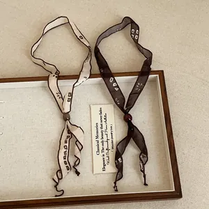 Detail view of beige and brown printed ribbon scarf necklaces in a wooden tray