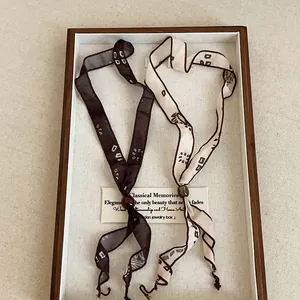 Two minimalist printed ribbon scarf necklaces showcased in a vintage wooden tray display.