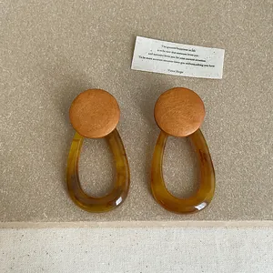 Detail view of amber resin earrings with geometric wood studs and teardrop shape