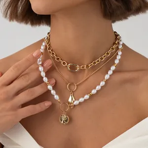 Gros plan d'un collier de perles baroques avec médaille d'or et pendentif main