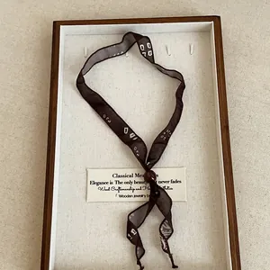 Close-up of a brown printed silk ribbon necklace in a wooden display tray.