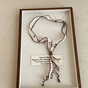 Detail view of a minimalist printed ribbon scarf necklace showcased in a wooden jewelry tray