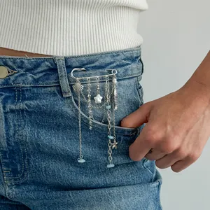 Détail d'une broche épingle à nourrice avec coquillages et turquoise sur une poche de jean.