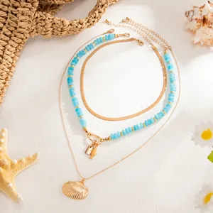 Détail du collier de perles en résine bleue et du pendentif coquillage doré chic.