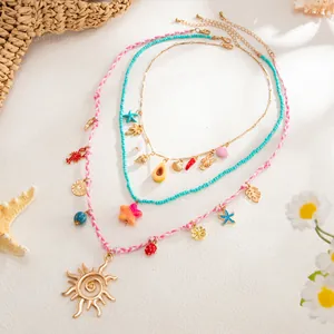 Détail de colliers superposés en perles et tressés avec pendentifs soleil et mer