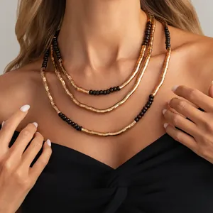 Close-up detail of a layered necklace featuring textured gold metal and dark brown beads.