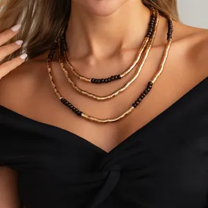 Detail of three-layer layered necklace with gold metal tubes and dark wood beads