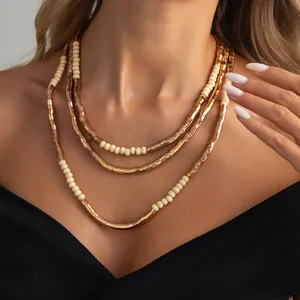 Close-up detail of stylish layered metallic gold and cream bead necklaces on female model