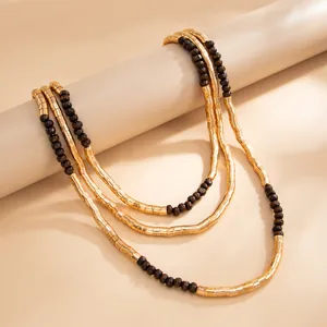 Close-up of textured gold metallic tubes and dark brown beads on a layered necklace.