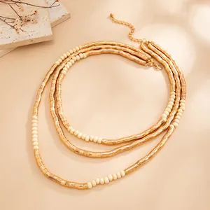 Detailed view of textured gold metal tubes and cream seed bead layered necklace.