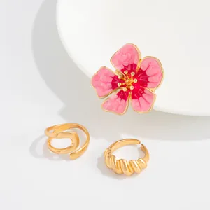 Gedetailleerd zicht op roze emaille bloem en gouden spiraal teenringen op witte basis