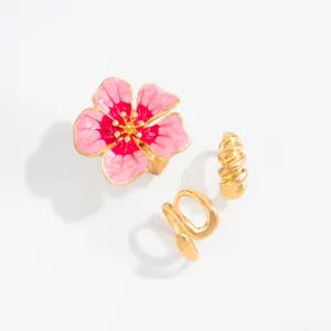 Detailweergave van de roze emaille bloem en goudkleurige gedraaide teenringenset