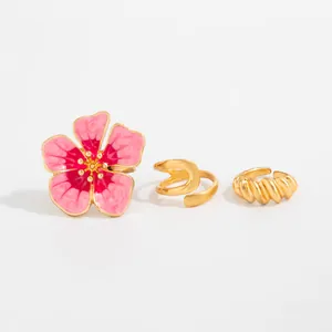 Detailweergave van roze emaille bloem en goud gedraaide open teenringen voor de zomer.
