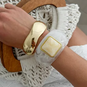 Close-up detail of vintage gold wavy bangle and marbled white acrylic square bracelet