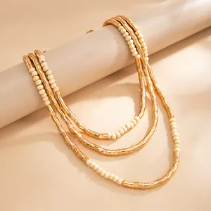 Close-up of bohemian layered necklace featuring textured gold tubes and cream beads.