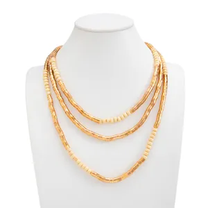 Detail of layered necklace with golden metallic tubes and cream beads on a white mannequin.