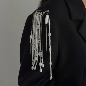 Close-up of elegant long fringe brooch with white imitation pearl beads and silver chains.